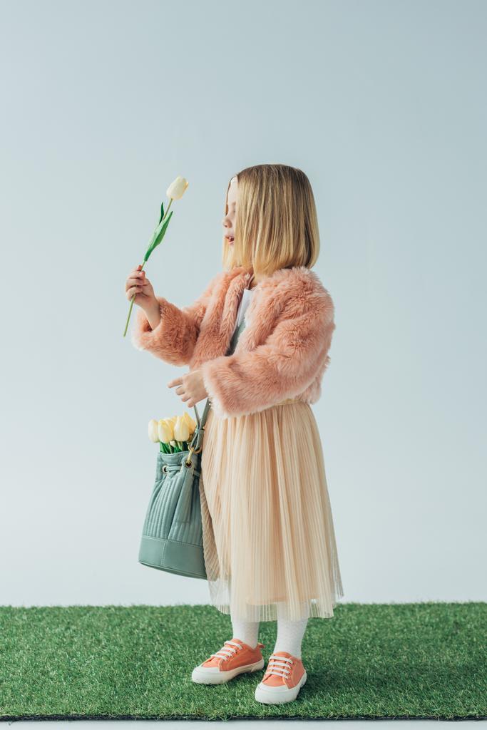 zaskoczony i słodkie dziecko z torba ogląda białego tulipana na szarym tle - Zdjęcie, obraz