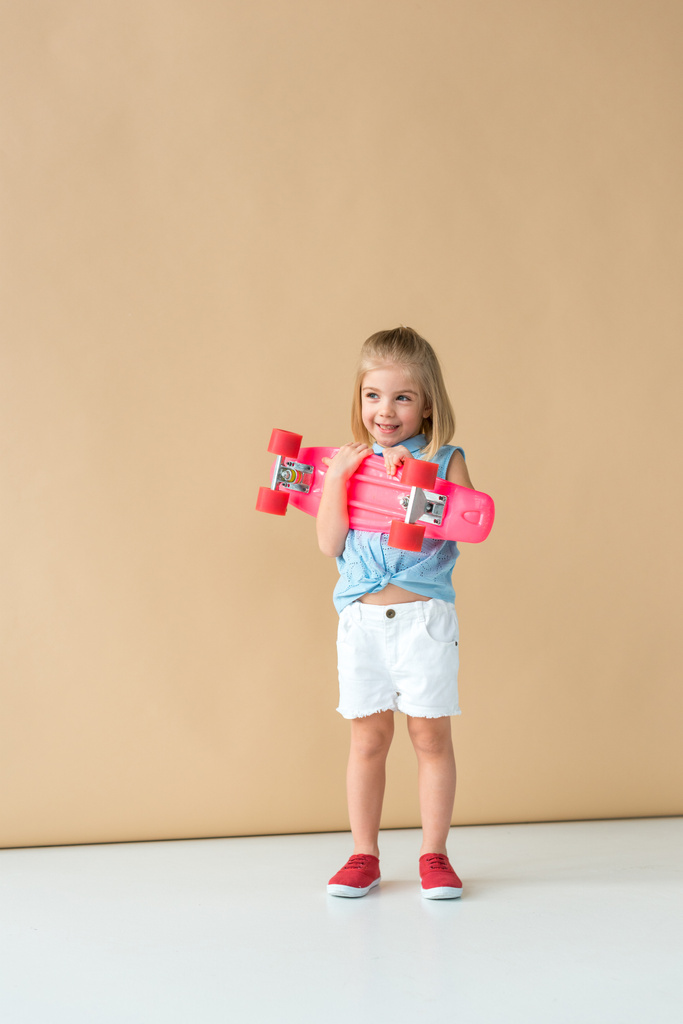 シャツとショーツ ベージュ色の背景にピンクのペニーのボードを持って笑顔でかわいい子供  - 写真・画像