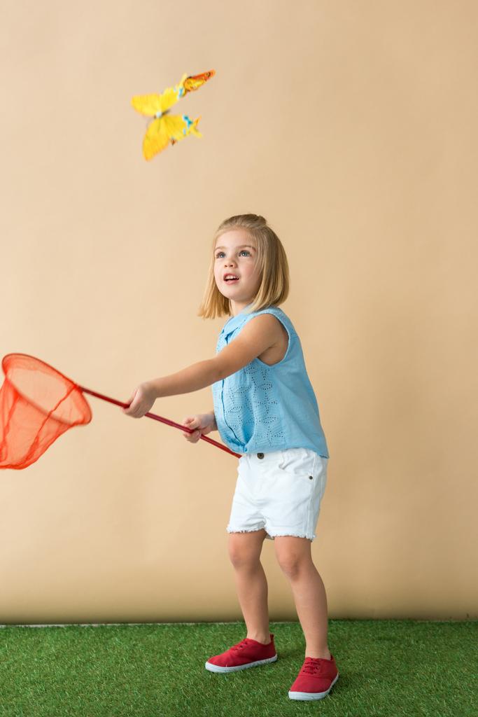милый ребенок ловит бабочку с сеткой красной бабочки на бежевом фоне
  - Фото, изображение