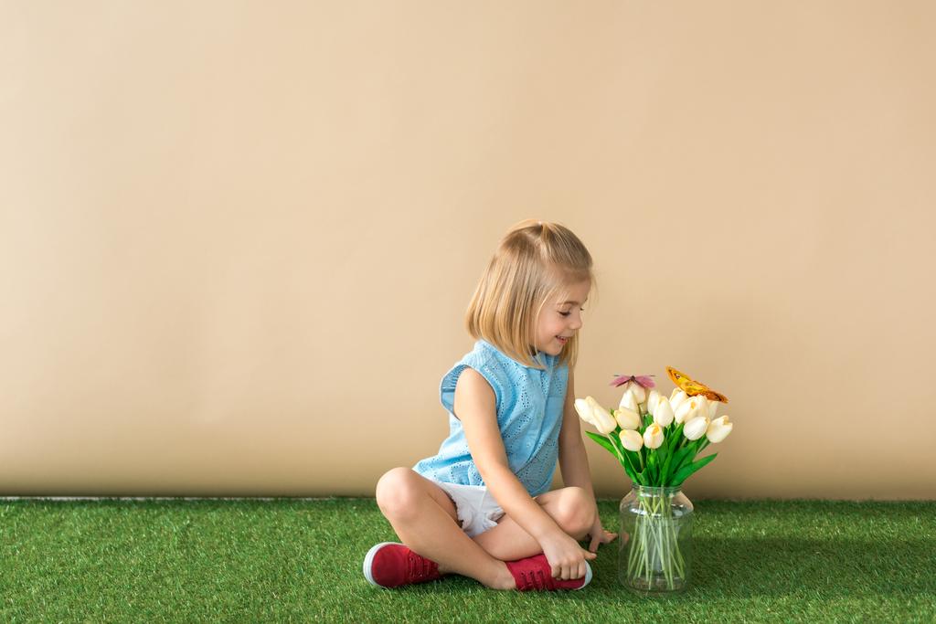 šťastné dítě sedí se zkříženýma nohama a při pohledu na květiny a motýly - Fotografie, Obrázek