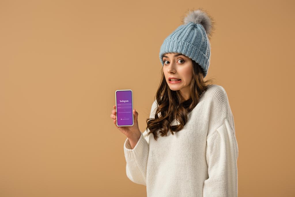 Chica atractiva confusa sosteniendo teléfono inteligente con aplicación instagram en la pantalla aislada en beige
 - Foto, imagen