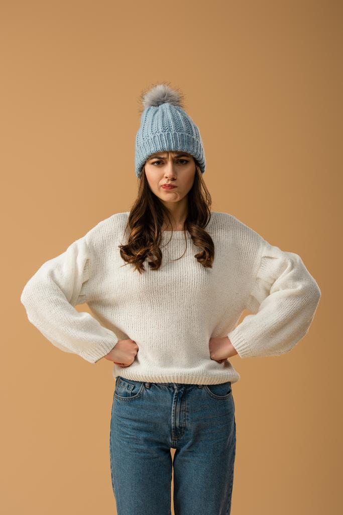 Sceptyczny brunetka dziewczyna w stojący biały sweter z ramionami okrakiem na beżowym tle - Zdjęcie, obraz