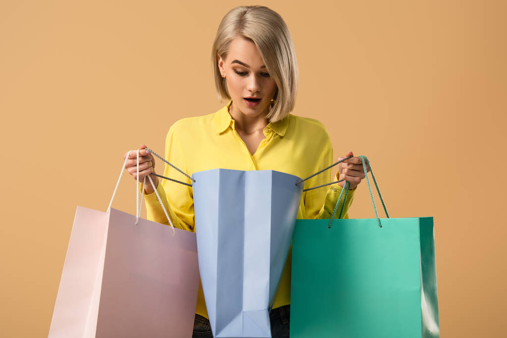 Schockierte blonde Frau schaut in Einkaufstasche vereinzelt auf Beige - Foto, Bild