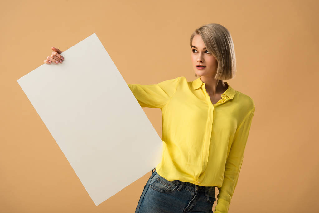 verträumte junge Frau in gelbem Hemd mit leerem Plakat auf beigem Hintergrund - Foto, Bild