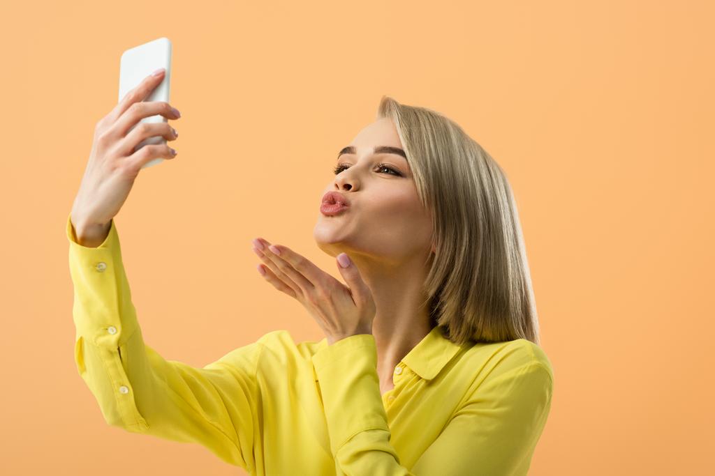 Linda menina loira enviando beijo de ar enquanto toma selfie isolado na laranja
 - Foto, Imagem