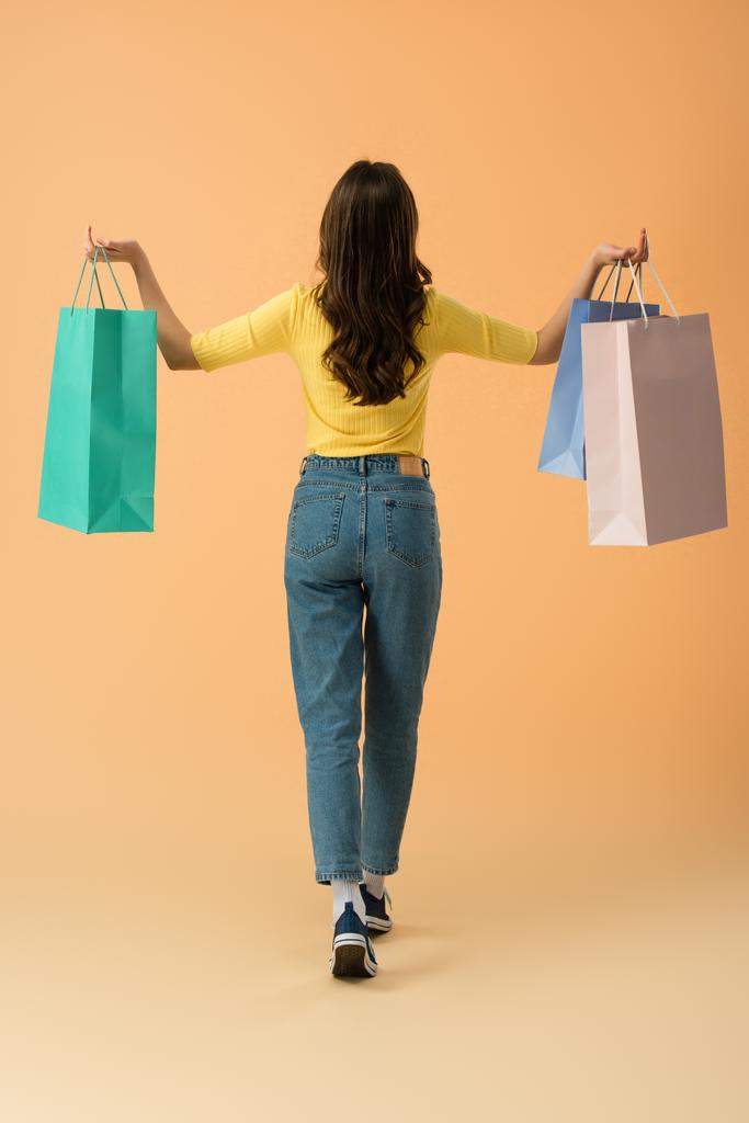Visão traseira da mulher morena em jeans segurando sacos de compras no fundo laranja
 - Foto, Imagem