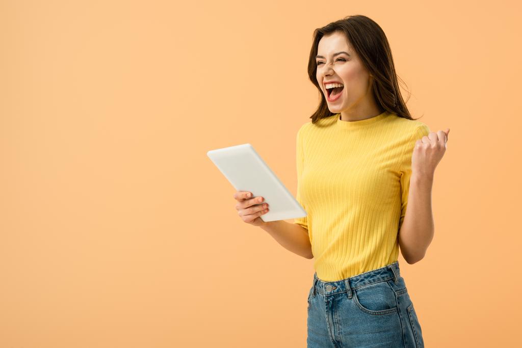 Excited brunette girl holding digital tablet and laughing isolated on orange - Photo, Image