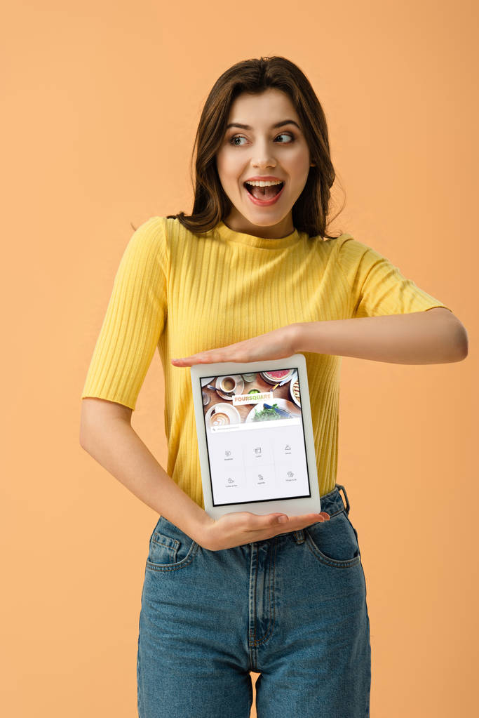 Mujer morena feliz sosteniendo tableta digital con aplicación cuadrada en la pantalla aislada en naranja
 - Foto, imagen