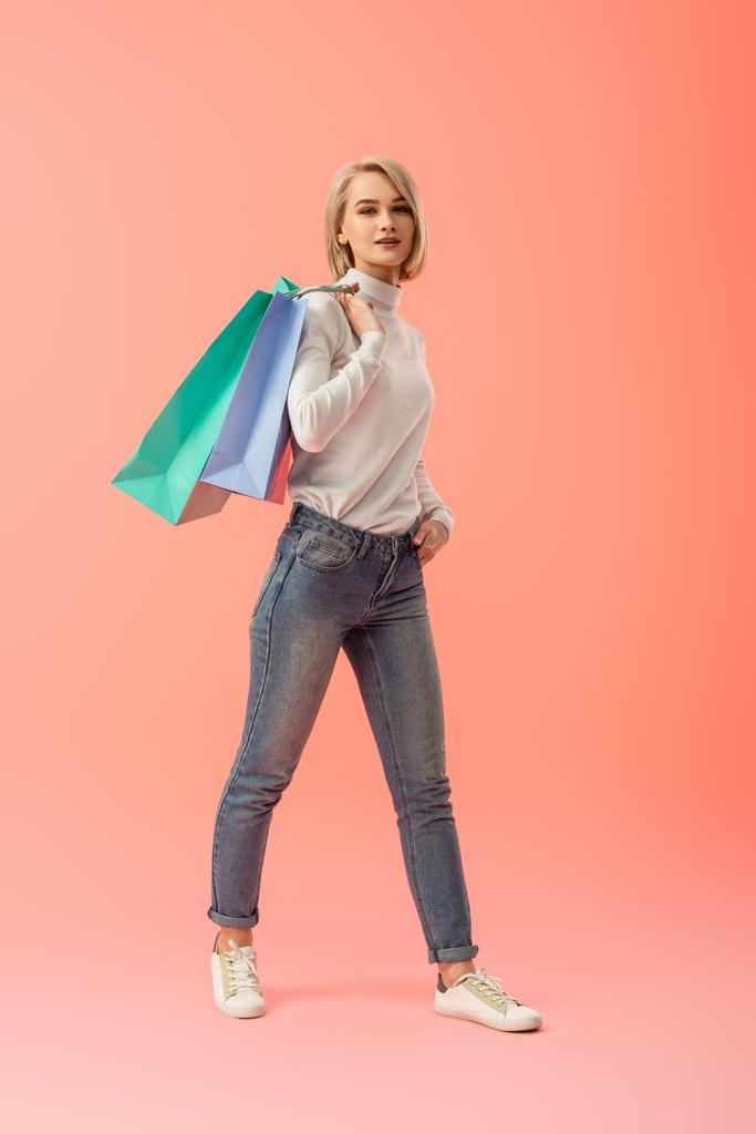 attractive blonde young woman holding shopping bags on pink background  - Photo, Image