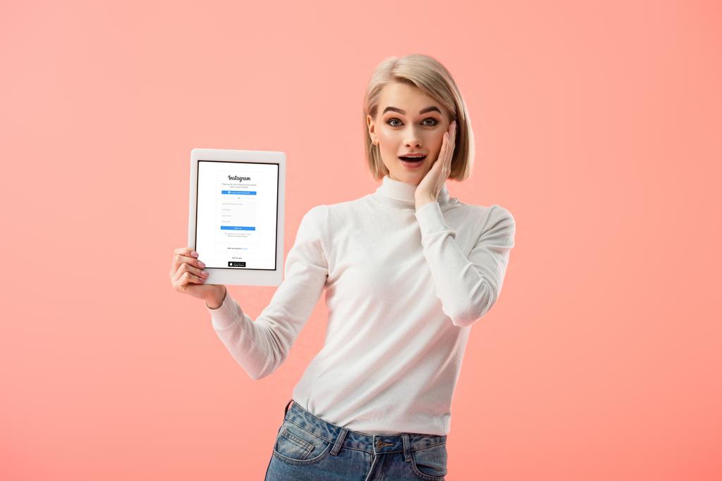 verbaasd blonde vrouw met digitale tablet met instagram app op scherm geïsoleerd op roze  - Foto, afbeelding