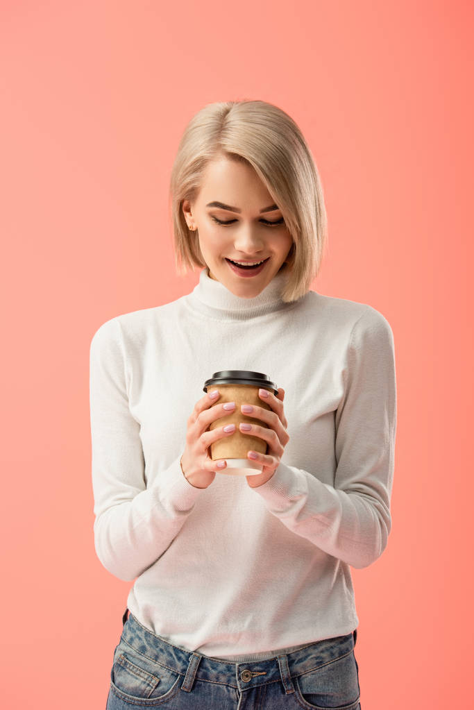 surpris fille blonde regardant tasse en papier avec boisson isolé sur rose
  - Photo, image