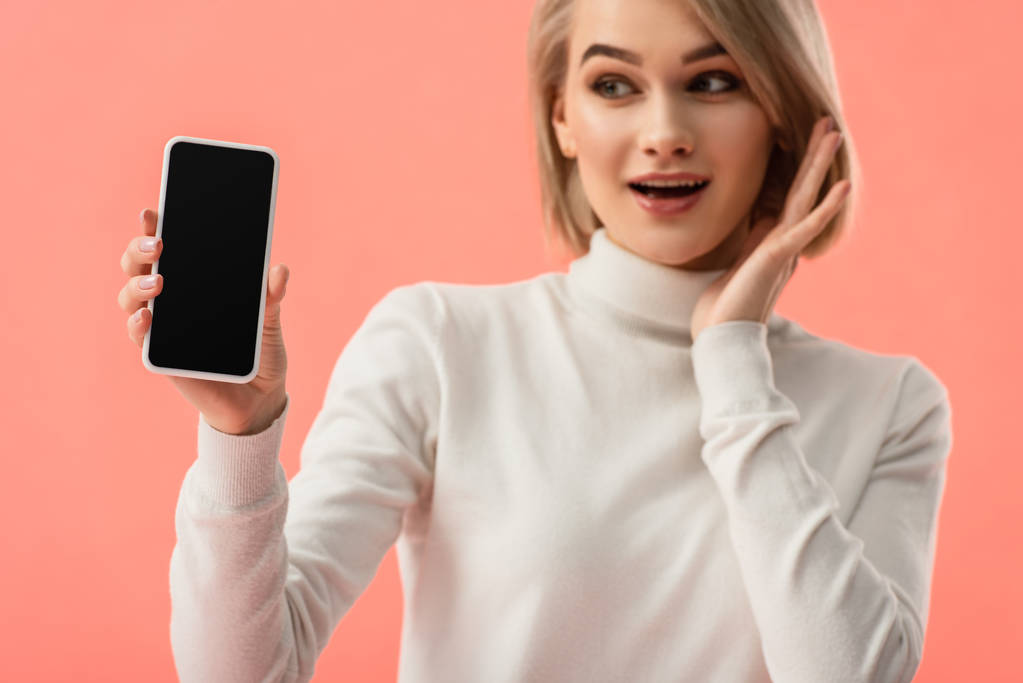 вибірковий фокус шокованої молодої блондинки, що тримає смартфон з порожнім екраном ізольовано на рожевому
  - Фото, зображення
