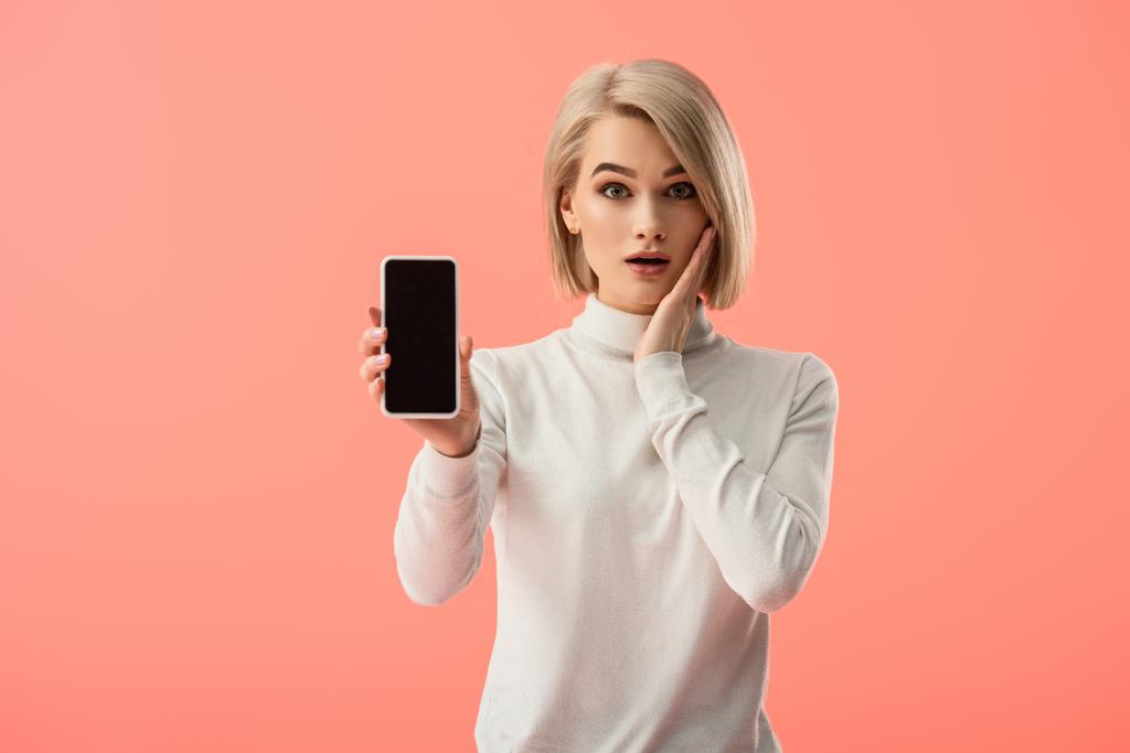 zszokowany młoda kobieta blonde, trzymając smartfon z pustego ekranu na różowym tle  - Zdjęcie, obraz