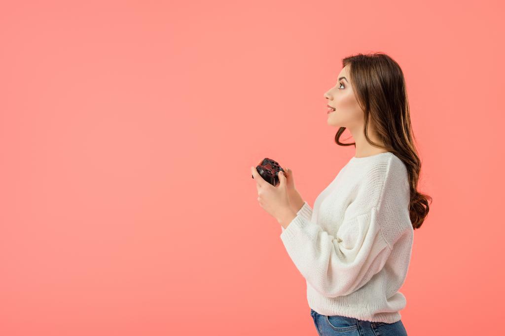 side view of surprised girl holding joystick while standing isolated on pink  - Photo, Image