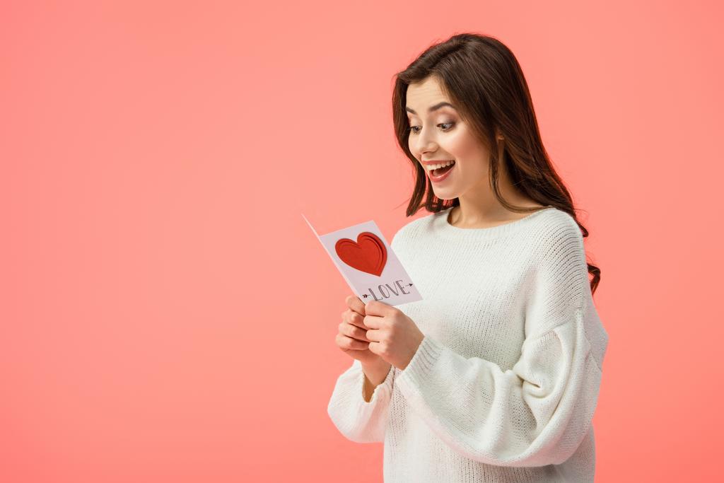 meglepett és vonzó fiatal nő gazdaság kártyát a szerelem betűk elszigetelt rózsaszín   - Fotó, kép