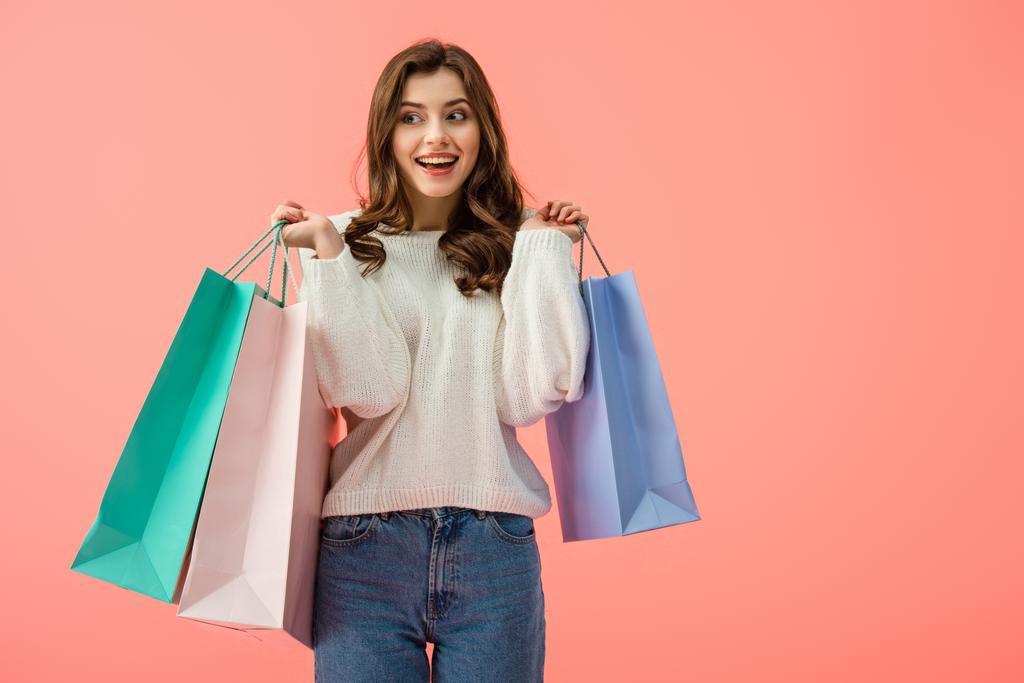 smiling and attractive woman in white sweater holding shopping bags isolated on pink - Photo, Image
