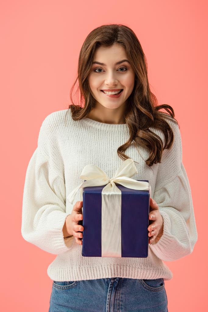 smiling and attractive woman in white sweater holding gift box isolated on pink  - Photo, Image