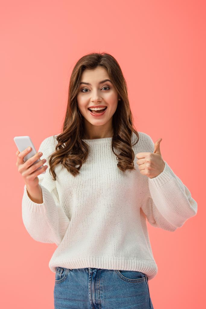 mulher sorridente e atraente com polegar para cima segurando smartphone isolado em rosa
 - Foto, Imagem