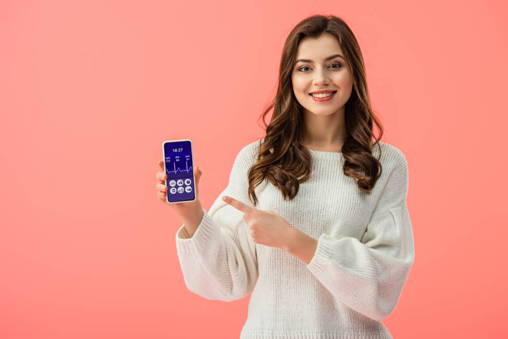 женщина в белом свитере указывая пальцем на смартфон с приложением здоровья на экране изолированы на розовый
  - Фото, изображение