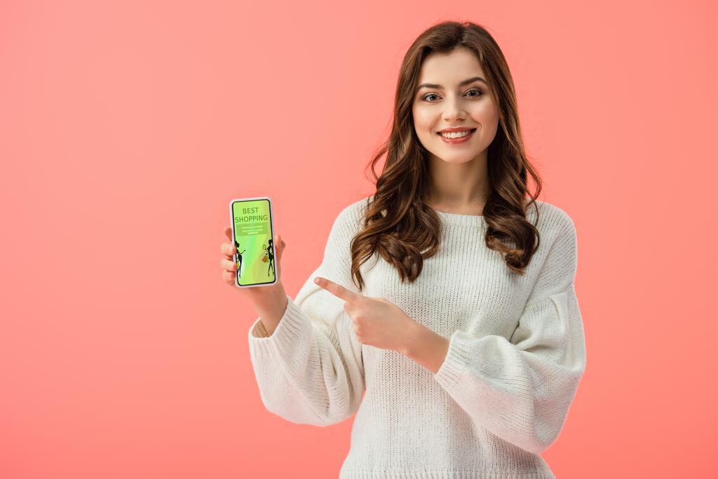 mujer en suéter blanco apuntando con el dedo al teléfono inteligente con la mejor aplicación de compras en la pantalla aislada en rosa
  - Foto, imagen