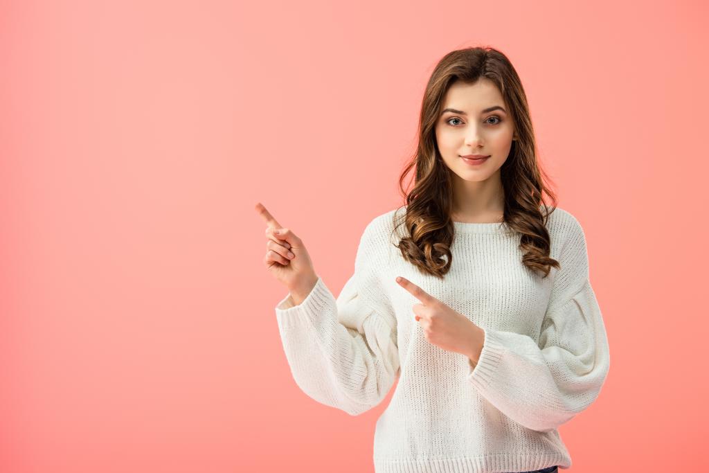 smiling and beautiful woman in white sweater pointing with fingers isolated on pink - Photo, Image