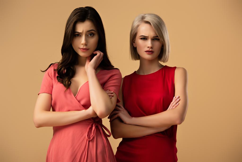 upset beautiful women in red dresses with crossed arms looking at camera isolated on beige - Photo, Image