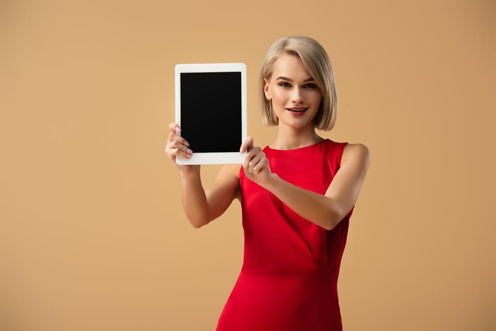 krásná žena v červených šatech, držící digitální tabletu s prázdnou obrazovkou izolované na béžové - Fotografie, Obrázek