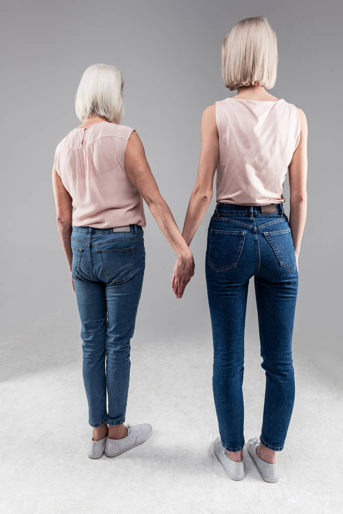 Rubia de pelo corto niñas de pie con su vieja madre y sosteniendo su mano
 - Foto, imagen