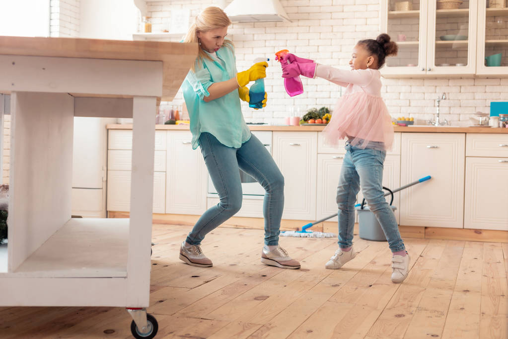 Mère et fille s'amusent avec un spray nettoyant dans la cuisine
 - Photo, image