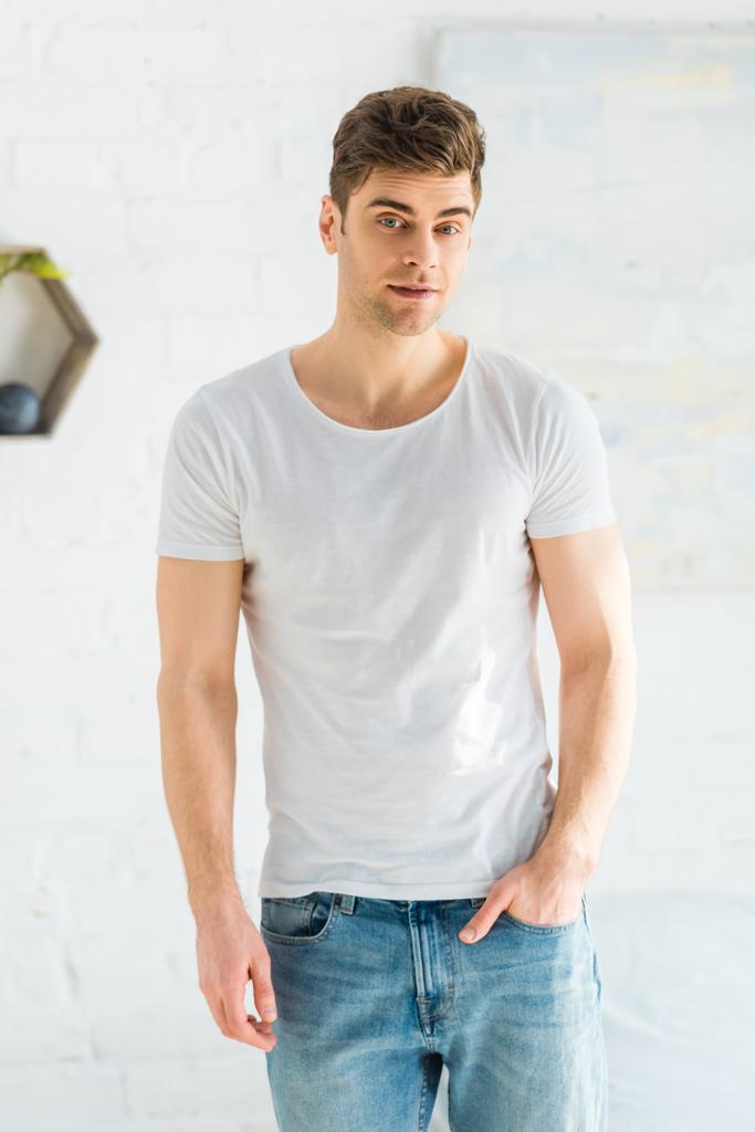 knappe man in wit t-shirt en jeans permanent op witte achtergrond - Foto, afbeelding