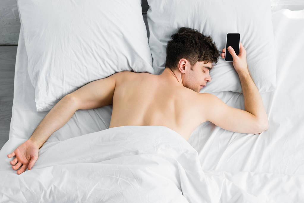 όμορφος άνθρωπος που κοιμάται κάτω από κουβέρτα κοντά σε smartphone με κενή οθόνη για κακή - Φωτογραφία, εικόνα