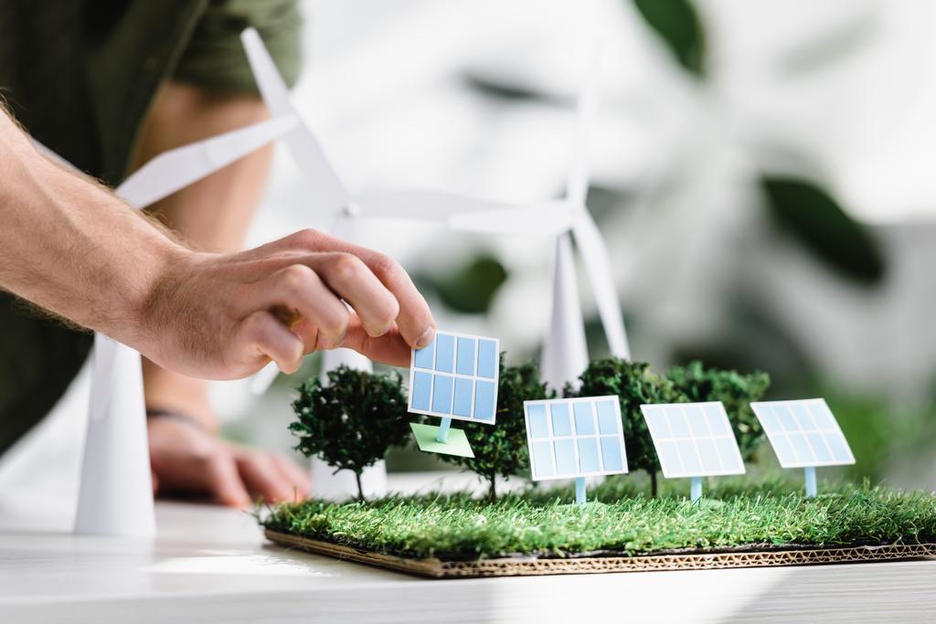 オフィスでテーブルの芝生の上の太陽電池パネルのモデルを置く男のビューをトリミング - 写真・画像