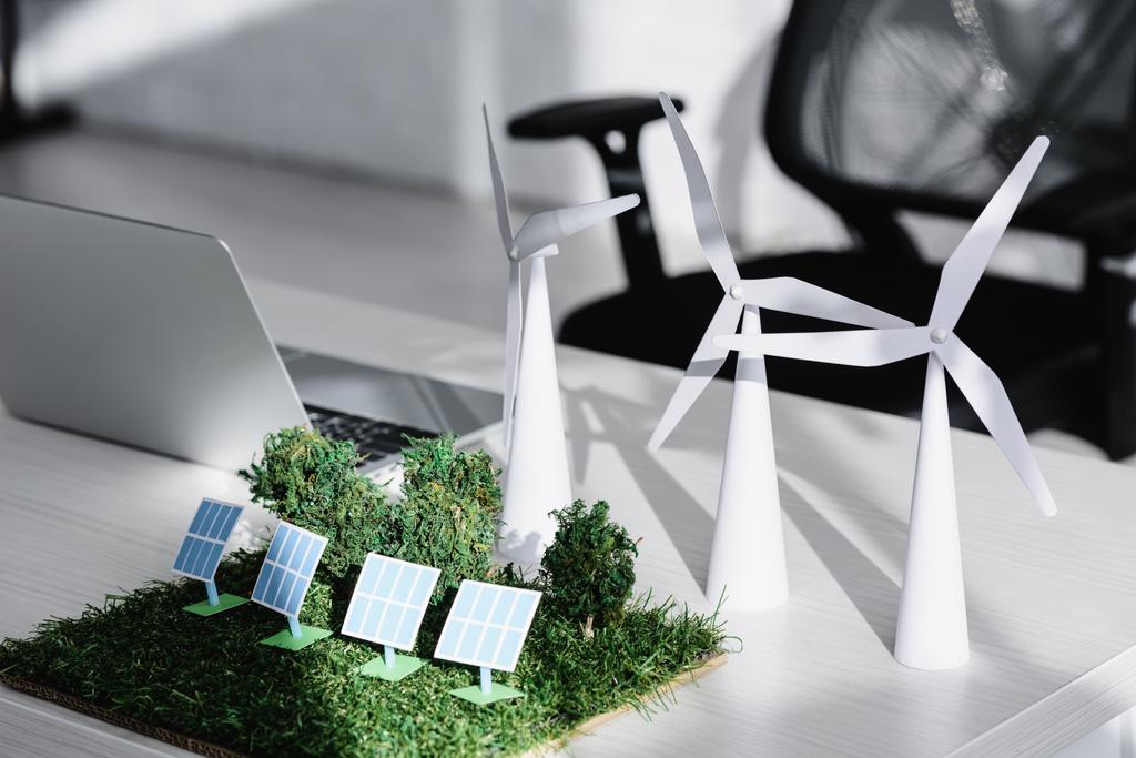 стул рядом стол с ноутбуком, деревья, ветряные мельницы, солнечные батареи модели на траве в офисе
 - Фото, изображение