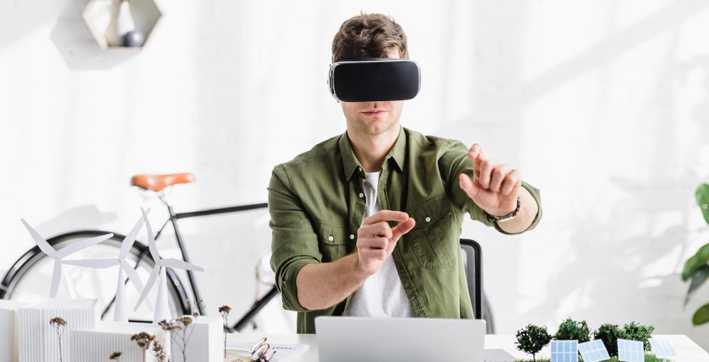 Architekt in Virtual-Reality-Headset am Tisch mit Laptop und Bäumen, Solarmodellen im Büro - Foto, Bild