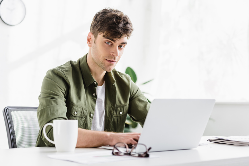 uomo in camicia verde seduto a tavola con computer portatile e digitando in ufficio
 - Foto, immagini