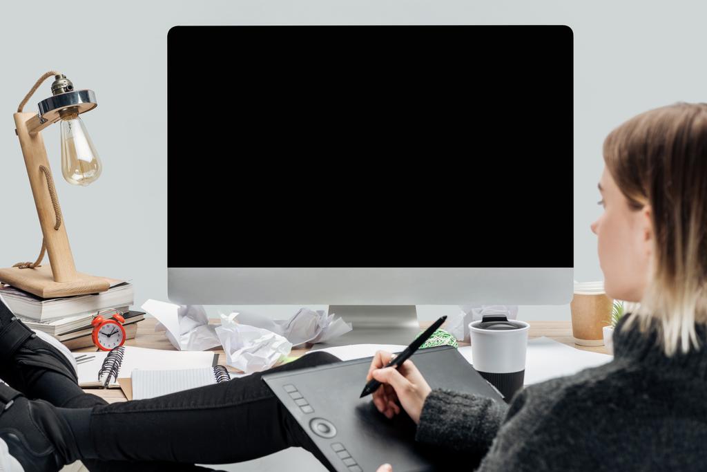 дівчина сидить на безладному робочому місці з ногами на столі і використовує графічний планшет ізольований на сірому
 - Фото, зображення