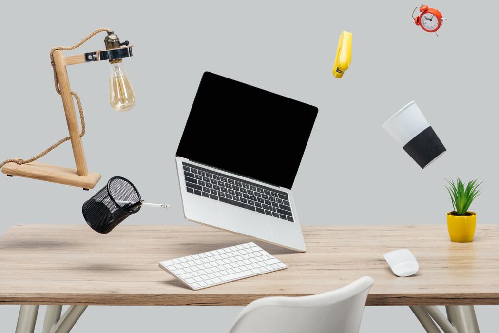 Laptop mit leerem Bildschirm und Schreibwaren, die in der Luft schweben, am Arbeitsplatz isoliert auf grau - Foto, Bild