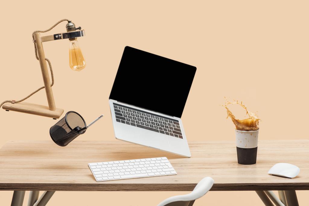 Laptop mit leerem Bildschirm und Lampe schwebt in der Luft über dem Arbeitsplatz mit Thermomug mit Kaffeesatz isoliert auf beige - Foto, Bild