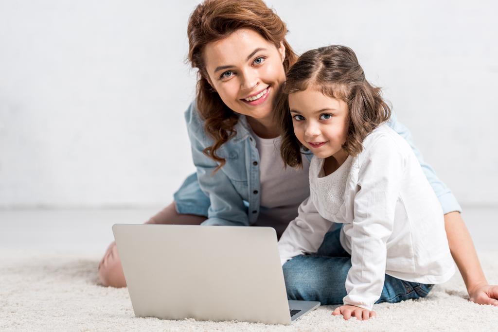 Sorrindo mãe e filha sentados no chão e usando laptop no branco
  - Foto, Imagem