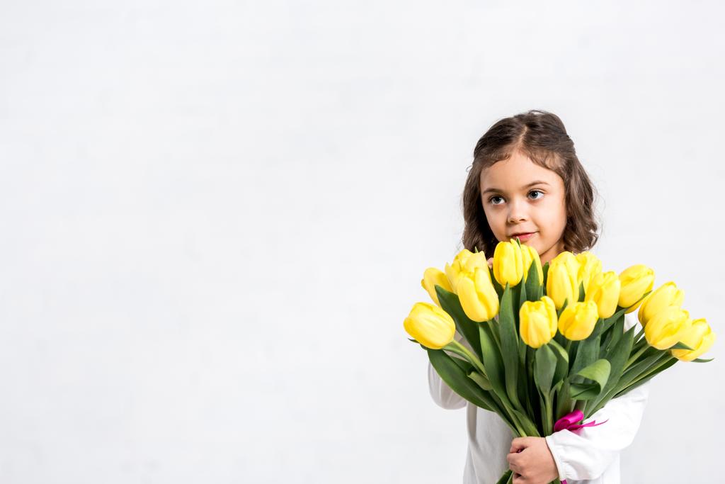 Rozkošné dítě drží kytici tulipánů a při pohledu od izolované na bílém - Fotografie, Obrázek