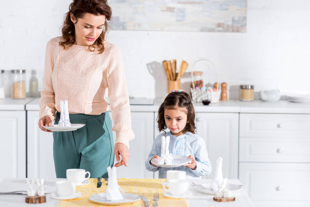 Kręcone matki i przedszkolak córka serwowania tabeli w kuchni - Zdjęcie, obraz