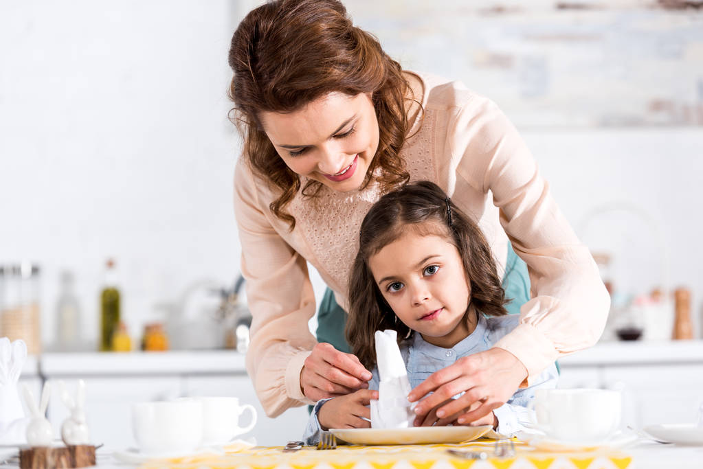 Uśmiechnięte matki i córeczka składane serwetki w kuchni - Zdjęcie, obraz