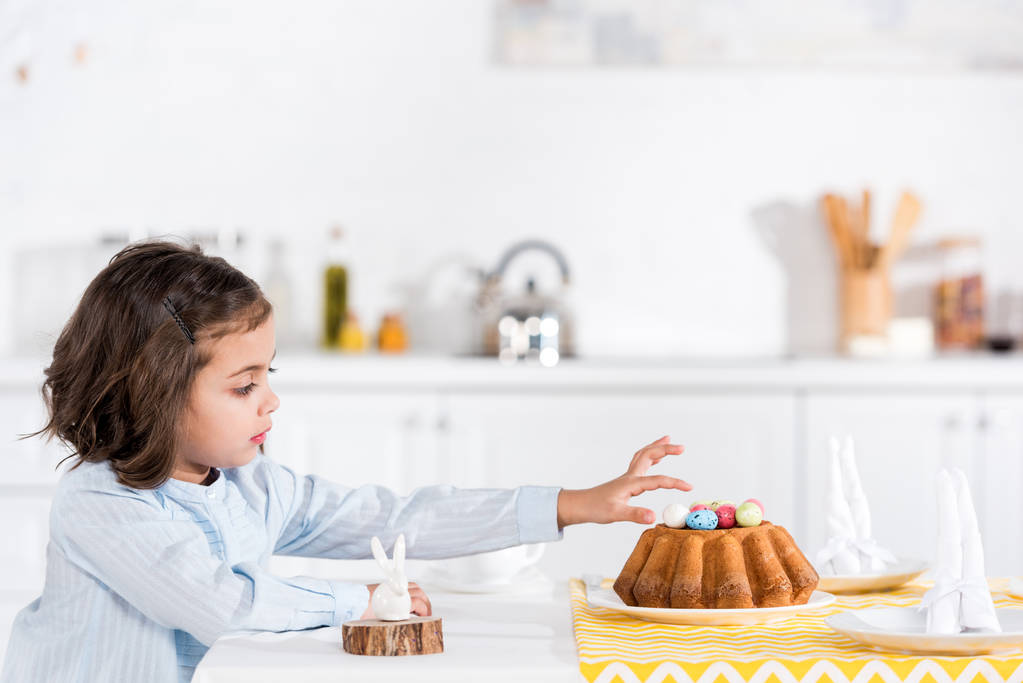 Чарівна дитина прикрашає великодній хліб з розфарбованими яйцями на кухні
 - Фото, зображення