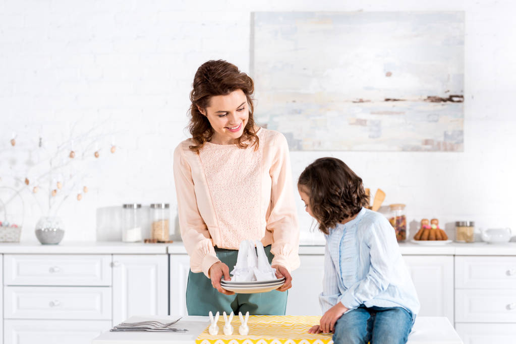 Улыбающаяся мать показывает сложенные салфетки дочери на кухне
 - Фото, изображение