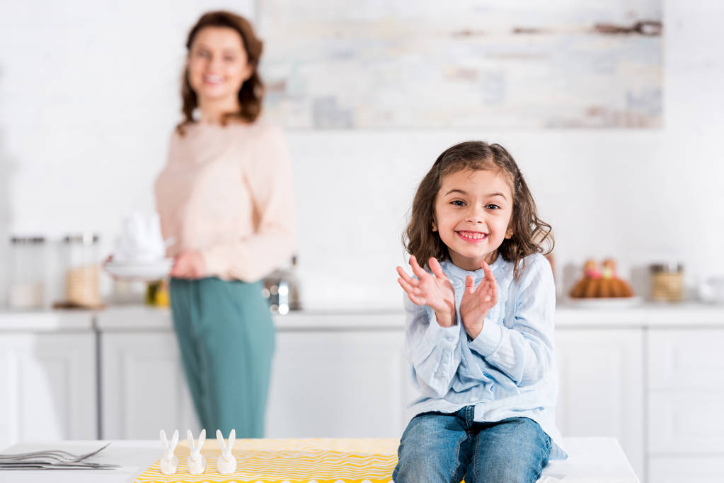 Criança alegre sentada na mesa e sorrindo na cozinha
 - Foto, Imagem