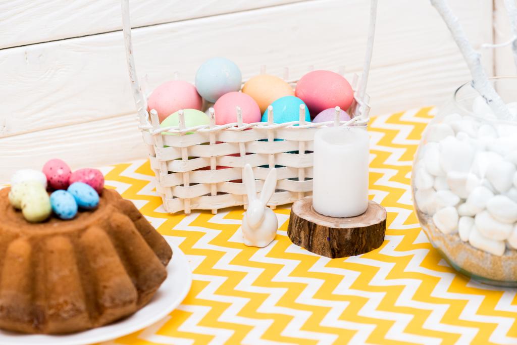 Pastel de Pascua, huevos pintados, vela y conejo de cerámica en la mesa
 - Foto, imagen
