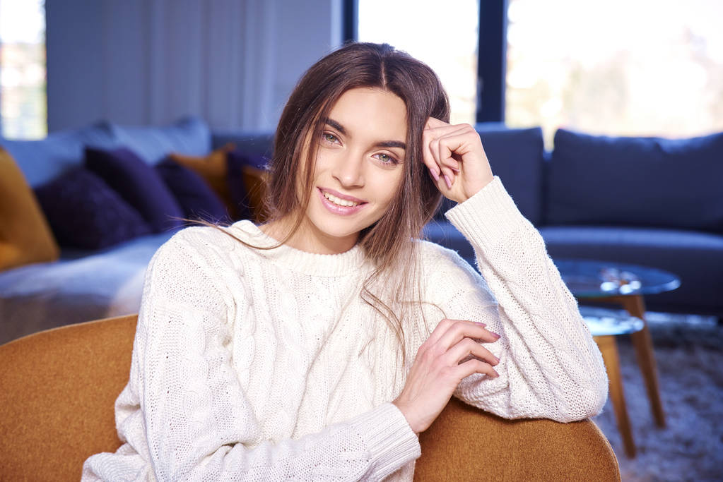 Πορτρέτο του όμορφη νεαρή κοπέλα φορώντας ρούχα casual και χαμογελαστός ενώ χαλαρώνετε στον καναπέ στο σπίτι.  - Φωτογραφία, εικόνα