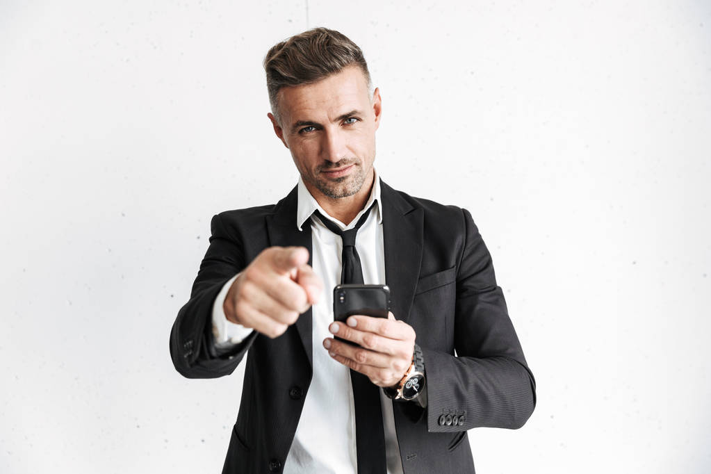 ビジネスの男性のポーズを指差しする携帯電話を使用して白い壁バック グラウンドを分離. - 写真・画像