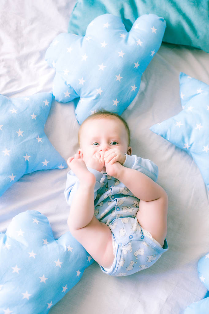 Roztomilé batole chlapce na posteli doma obklopen modré polštáře - Fotografie, Obrázek