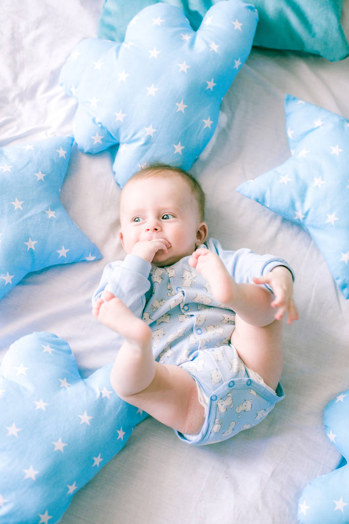 Lindo niño en la cama en casa rodeado de almohadas azules
 - Foto, imagen